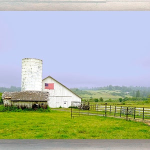May include: A white farmhouse with a silo and an American flag flying on the side, set against a green grassy field and a blue sky with clouds.