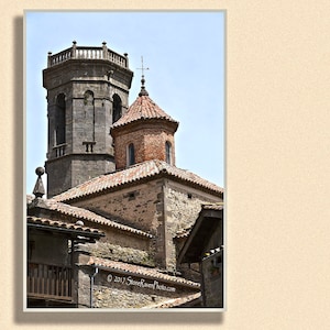 Peut inclure: Une vue rapprochée d'un bâtiment en pierre avec une haute tour et une structure plus petite au toit rouge. La tour a un sommet pointu et une série de fenêtres. La structure plus petite a une croix au sommet et une fenêtre ronde.