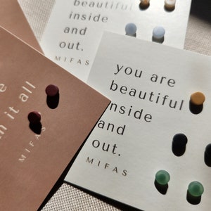 May include: Four cards with different colored and textured round earrings and the text "you are beautiful inside and out." on each card.
