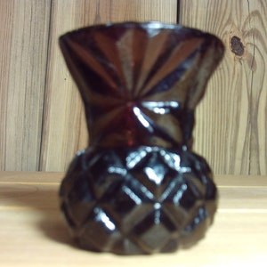 Puede incluir: Un peque&ntilde;o jarr&oacute;n de vidrio rojo oscuro con un patr&oacute;n de diamante. El jarr&oacute;n tiene una boca ancha y una base estrecha.