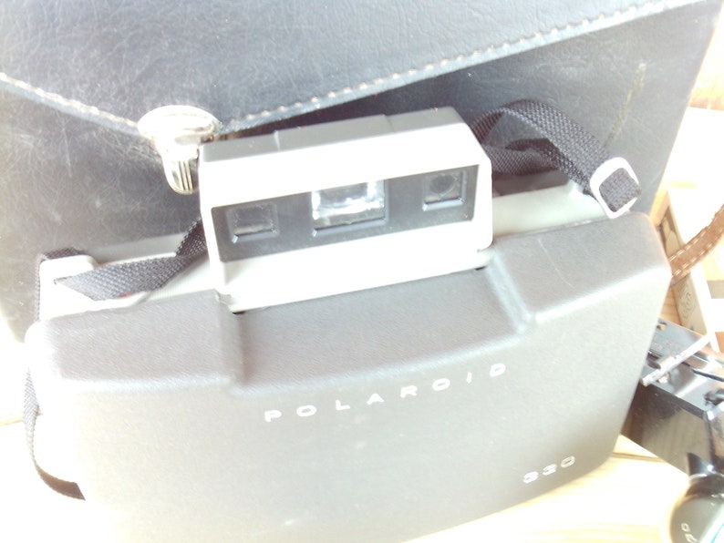 May include: A gray Polaroid camera with a black strap and the text "POLAROID 930" on the front.