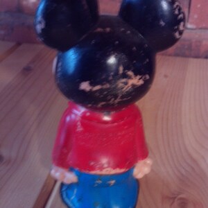 May include: A black and red plastic Mickey Mouse figurine with large ears and blue pants. The figurine has a worn and faded appearance.