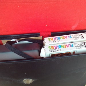 May include: A black leather case with a silver latch, containing two boxes of Sylvania M3 Blue Dot Flashbulbs.