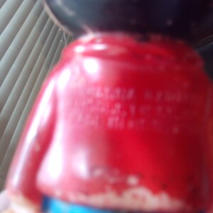 May include: A red plastic figurine of a cartoon character wearing a red shirt and blue pants. The figurine has black hair and a black face. The text "Made in China" is visible on the back of the figurine.