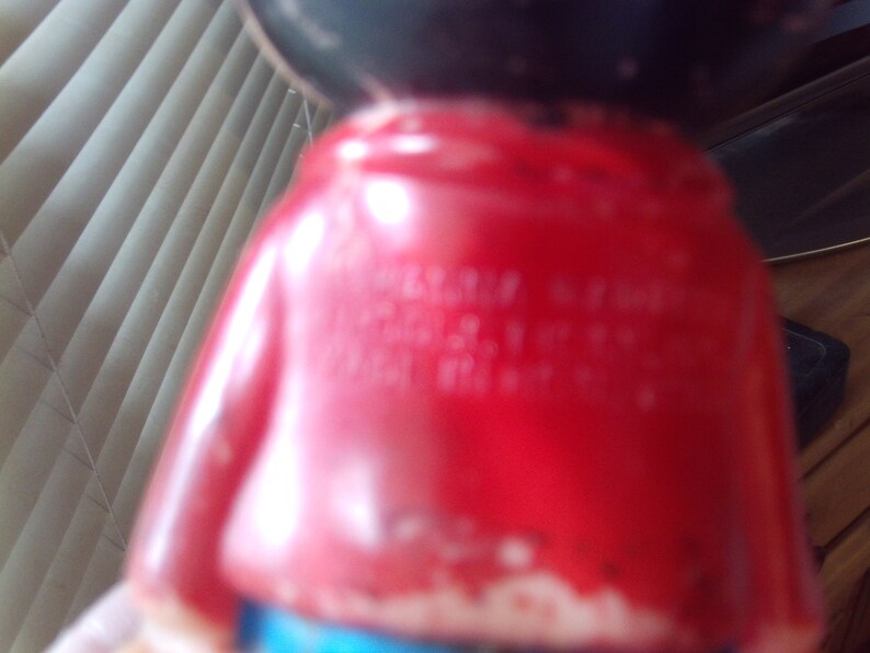 May include: A red plastic figurine of a cartoon character wearing a red shirt and blue pants. The figurine has black hair and a black face. The text "Made in China" is visible on the back of the figurine.