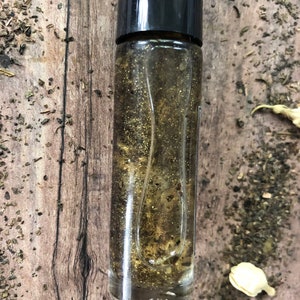 May include: A clear glass roller bottle with a black cap filled with a golden liquid and glitter.