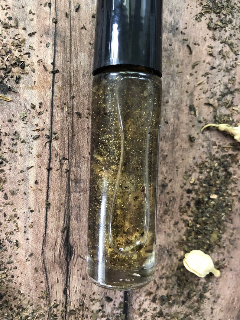 May include: A clear glass roller bottle with a black cap filled with a golden liquid and glitter.