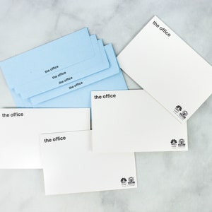 May include: A stack of light blue envelopes with the text "the office" printed on each one. There are also three white envelopes with the same text and a logo on the bottom right corner.