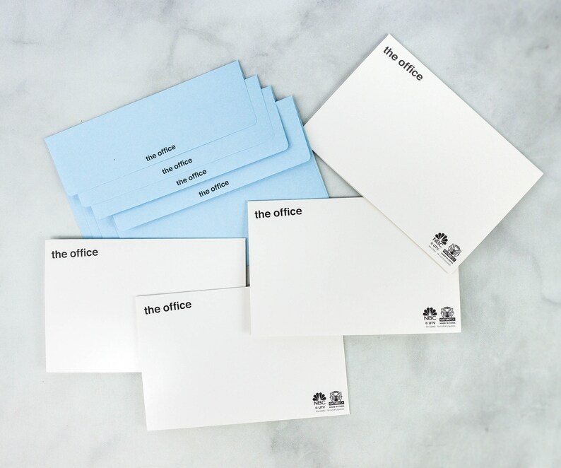 May include: A stack of light blue envelopes with the text "the office" printed on each one. There are also three white envelopes with the same text and a logo on the bottom right corner.