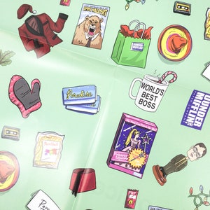 May include: A green and white patterned wrapping paper with various images including a red Santa suit, a bear, a coffee mug with the text "World's Best Boss", a bag with the text "Dunder Mifflin", a pink unicorn toy, and a red fez.