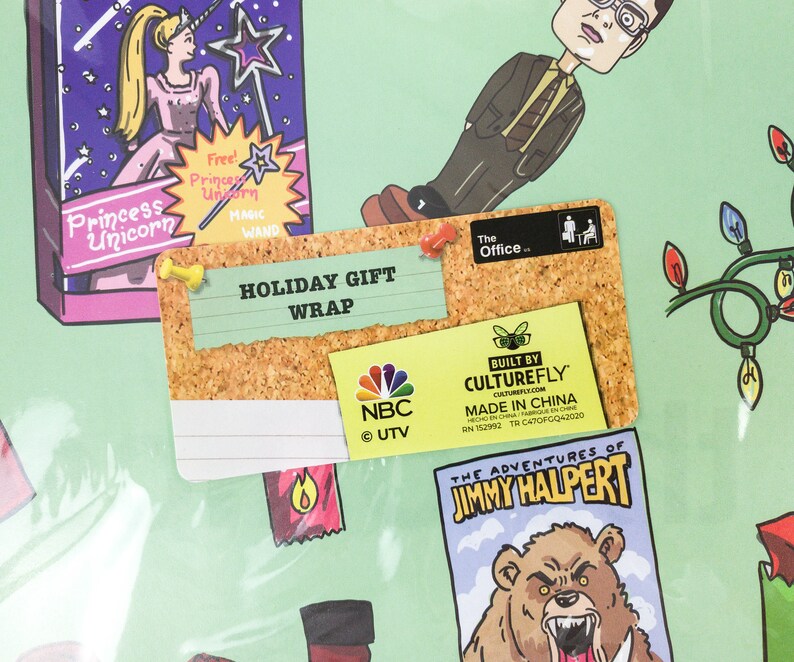 May include: A corkboard with a white note that says "HOLIDAY GIFT WRAP" and a smaller note that says "BUILT BY CULTUREFLY" with the company website and "MADE IN CHINA". There is a small NBC logo and a sticker that says "The Office."
