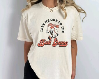 May include: A cream coloured t-shirt with a vintage baseball graphic and the text "Take me out to the ball game".