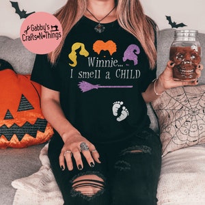 May include: Black t-shirt with a graphic of the Sanderson sisters from Hocus Pocus. The text "Winnie... I smell a CHILD" is printed on the shirt.