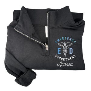 May include: Black zippered sweatshirt with a white graphic of a medical caduceus symbol with the text "Emergency Department" and the name "Andrea" underneath.