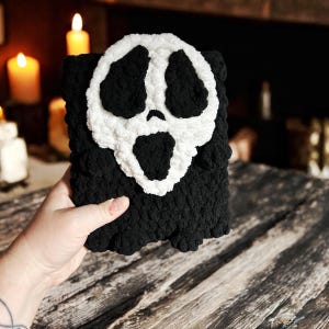 May include: A black and white crocheted ghost pillow with a scary face. The pillow is made of soft, fluffy yarn and is perfect for Halloween decor.