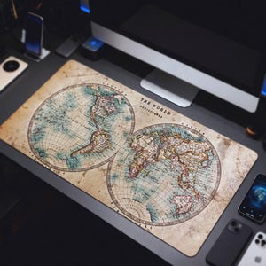 May include: A rectangular desk mat featuring a vintage world map design. The map is divided into two hemispheres, with detailed illustrations in shades of blue, brown, and beige. The text "THE WORLD HEMISPHERES" is printed on the mat.