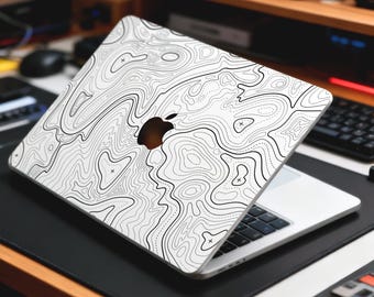 May include: A white laptop with a topographic map design on the lid. The black and white pattern features contour lines and symbols. The laptop has a silver body and a black keyboard. The Apple logo is visible.
