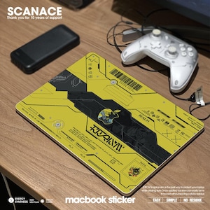 May include: A yellow and black laptop skin with a futuristic design and the text "SCANACE" and "macbook sticker". The skin features a black and white illustration of a robot with the text "ROZAIYVI" in Japanese characters.