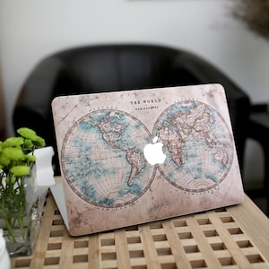 Puede incluir: Un ordenador portátil con un diseño de mapa del mundo de estilo vintage. El mapa muestra océanos azules y continentes marrones, con el texto "THE WORLD HEMISPHERES" en la parte superior. El logotipo de Apple es visible.