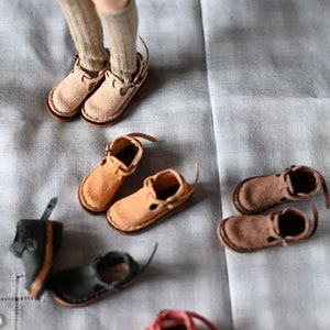 K&ouml;nnte beinhalten: Eine Sammlung von Miniatur-Lederschuhen in verschiedenen Farben, darunter Braun, Beige, Schwarz und Rot. Die Schuhe haben verschiedene Stile, wie Stiefeletten, Sandalen und Mary Janes.