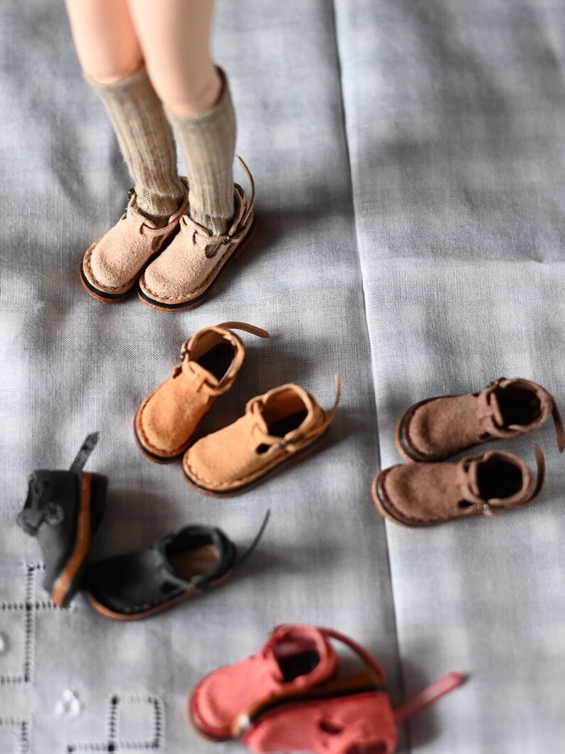 K&ouml;nnte beinhalten: Eine Sammlung von Miniatur-Lederschuhen in verschiedenen Farben, darunter Braun, Beige, Schwarz und Rot. Die Schuhe haben verschiedene Stile, wie Stiefeletten, Sandalen und Mary Janes.