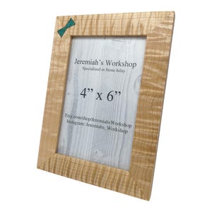 May include: A wooden picture frame with a natural wood finish and a turquoise bow tie inlay. The frame is 4 inches by 6 inches and is made by Jeremiah's Workshop, which specializes in stone inlay. The frame is for sale on Etsy and Instagram.