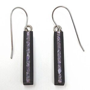 May include: A pair of dangle earrings with black wood and a thin strip of purple and white iridescent material. The earrings have silver hooks.