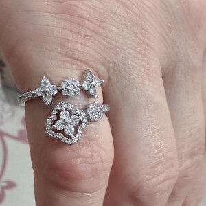 May include: Two silver rings with clear gemstones. One ring features a floral design with three flower-shaped clusters. The other ring has a cluster of small gemstones and three flower-shaped clusters.