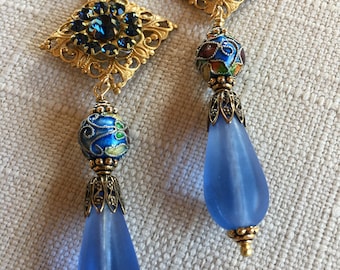 Könnte beinhalten: Ein Paar blaue Glas-Tropfenohrringe mit goldenen Filigranen und blauen Strasssteinen. Die Ohrringe haben eine blaue Emailleperle und einen tropfenförmigen blauen Glasanhänger.