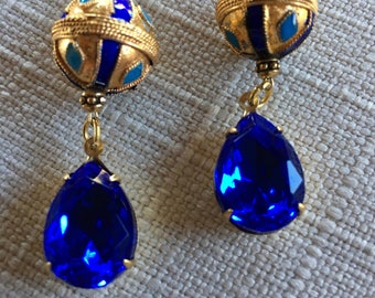 May include: A pair of gold dangle earrings with blue and turquoise enamel and a teardrop-shaped blue crystal.