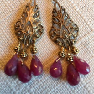 May include: Gold filigree earrings with dangling ruby red teardrop stones.
