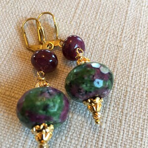 May include: Gold earrings with green and pink gemstone beads. The beads are faceted and have a metallic gold finish.