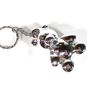 Op de afbeelding: Een zilveren teddybeer sleutelhanger met een zilveren ketting en een zilveren ring.