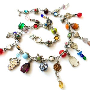 Könnte beinhalten: Mehrere silberfarbene Charm-Armbänder mit bunten Perlen und Anhängern. Die Armbänder weisen verschiedene Formen auf, darunter Herzen, Sterne und Tropfen, mit einer Vielzahl von farbigen Perlen und Edelsteinen. Auf weißem Hintergrund.
