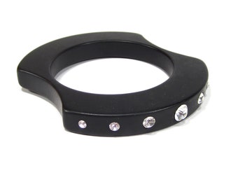 Op de afbeelding: Een zwarte bangle armband met een gebogen ontwerp en heldere strass steentjes.