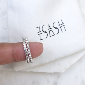 May include: Two silver beaded rings stacked on a finger. The rings are made of small, round beads.