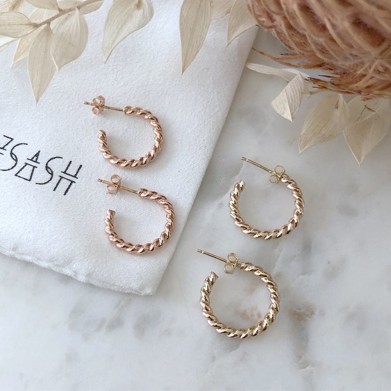 May include: Three pairs of gold-toned twisted hoop earrings on a white surface. The earrings are different sizes.