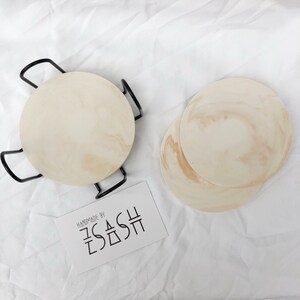 Puede incluir: Conjunto de cuatro posavasos redondos de color beige con un patr&oacute;n de m&aacute;rmol. Los posavasos est&aacute;n hechos a mano por "ZASH".