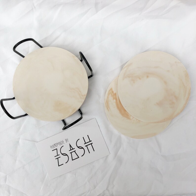 Puede incluir: Conjunto de cuatro posavasos redondos de color beige con un patr&oacute;n de m&aacute;rmol. Los posavasos est&aacute;n hechos a mano por "ZASH".