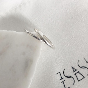 May include: Two silver rings, one with a hammered texture, are stacked on top of each other. The rings are on a white surface.