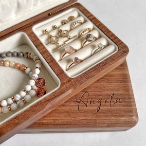 May include: A wooden jewelry box with a personalized inscription "Angela" on the lid. The box has a velvet interior with compartments for rings, earrings, and bracelets. The box is open and shows a variety of gold jewelry, including rings with gemstones, earrings, and bracelets.