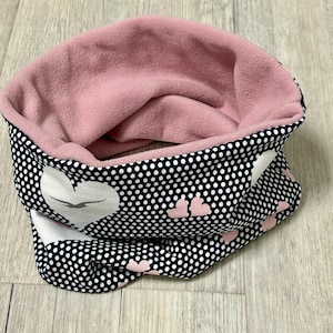 Könnte beinhalten: Ein gemütlicher Halsschmeichler mit weichem rosa Innenfutter und einer schwarz-weiß gepunkteten Außenseite. Die Außenseite hat weiße Herzformen mit einem Vogeldesign und kleine rosa Herzen. Dieses Winteraccessoire soll Sie warm halten.