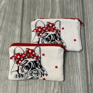 Könnte beinhalten: Zwei kleine, rechteckige Reißverschlusstaschen. Jede Tasche zeigt eine schwarz-weiße Illustration einer französischen Bulldogge mit einem roten Tupfen-Bandana. Rote Reißverschlüsse und rote Tupfen akzentuieren den cremefarbenen Stoff.