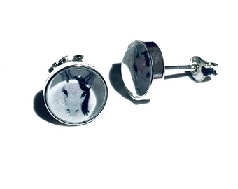 Könnte beinhalten: Silberne Ohrstecker mit einer schwarz-weißen Illustration eines Kuhgesichts. Die Ohrringe haben ein rundes, gewölbtes Design und einen Steckerverschluss. Das Gesicht der Kuh ist vor einem weißen Hintergrund abgebildet.