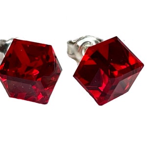 Könnte beinhalten: Ein Paar Ohrstecker mit facettierten, quadratisch geschliffenen, tiefroten Edelsteinen. Die Ohrringe haben einen silbernen Stiftverschluss. Die Edelsteine haben eine leuchtende, satte rote Farbe, und die Facetten erzeugen einen funkelnden Effekt.