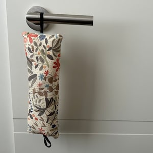 May include: A fabric door stop with a floral pattern, suspended from a silver door handle. The door stop has a cream base with a design of red, blue, and brown flowers and leaves. It has a black loop.