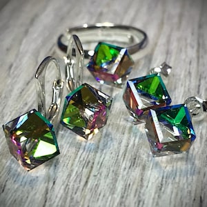 May include: A jewelry set featuring a ring and earrings with iridescent, cube-shaped crystals. The set includes leverback earrings and stud earrings. The crystals reflect a spectrum of colors, including green, blue, and purple, set against a silver metal.