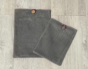 Peut inclure: Deux pochettes en velours côtelé gris de tailles différentes. Chaque pochette a une fermeture à bouton avec une boucle rouge. La plus grande pochette est rectangulaire, la plus petite est carrée.