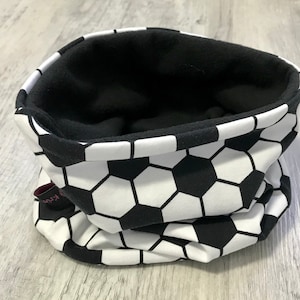 Könnte beinhalten: Ein schwarz-weißes Halstuch mit Fußballmuster. Die Außenseite zeigt ein sich wiederholendes Muster aus schwarzen Sechsecken auf weißem Hintergrund, während die Innenseite einfarbig schwarz ist. Das Halstuch ist zum Tragen um den Hals gedacht, um Wärme und Schutz zu bieten.