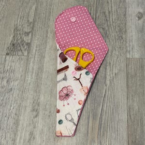 Può includere: Astuccio per forbici da cucito aperto con fodera a pois rosa e interno con stampa floreale. L'astuccio contiene un paio di forbici gialle. L'astuccio si chiude con un bottone rosa.
